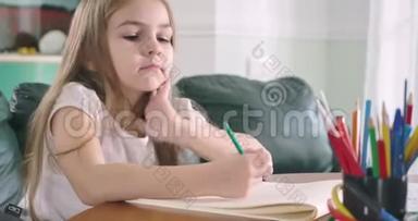 疲惫的白种人女孩坐在桌子旁做作业。 精疲力竭的孩子把头放在<strong>练习册</strong>和